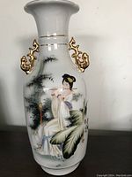 Full view of the vase showing hand-painted lady playing instrument and scenic background, gold trim handles.
