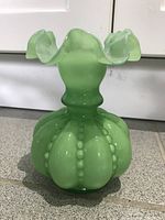 Front view of light green jadeite art glass vase showing ruffled top and bead-like detailing on rounded base.