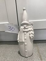 Front view of white porcelain snowman figurine with a tall pointy hat, scarf, and tree details showing relief snowflakes on its body.