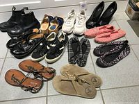 Overview of all women's shoes of various types and colors arranged on tile floor, showing full lot.