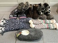 Photo showing all six pairs of slippers including two pairs of mukluk style moccasins and various holiday themed knit slippers.