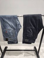 Both pairs of jeans hanging on a rack showing back pockets and overall condition.