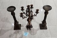Set of three metal candle holders arranged on floor, overview from front angle showing two tall single holders and one central multi-arm holder.