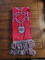 Folded red knit scarf with club and member insignia visible, displayed on wooden surface.