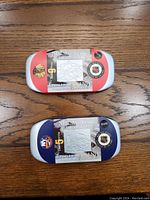 Two closed metal tins containing Canada Post NHL coin and stamp sets for Bobby Hull and Denis Potvin placed on a wooden surface.