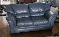 Front view of a dark genuine leather two-seat couch with cushioned armrests and backrest, placed on wooden floor.