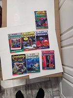 Seven first edition Goosebumps books by R.L. Stine laid out on white surface, showing colorful covers with horror-themed illustrations.