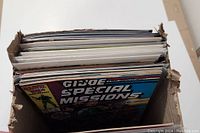 Photo of comic book lot in cardboard box showing G.I. Joe Special Missions comic on top