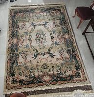 Photo of the full rug laid flat, showing floral ornate patterns and colors with some light wear.