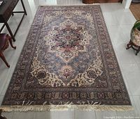 Full view of the large rectangular Oriental carpet on tiled floor surrounded by furniture, showing detailed central medallion and border design with fringes at one end.
