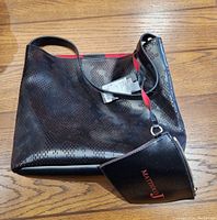Black Mattiolo J purse with perforated design and attached strap lying on wood floor, showing tags attached indicating new condition.