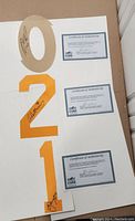 Large beige jersey number 0, orange number 2, and white number 1 arranged vertically on a flat surface. Each signed by a hockey player and alongside three Certificates of Authenticity.