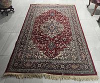 Full view of vintage oriental carpet laid out on floor showing overall pattern and fringed edges
