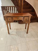 Full front view of wooden hallway side console table with three drawers, two small side drawers and one larger center drawer, all with metal ring pull handles.
