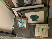 View showing four variously sized framed artworks leaning against a wall, along with the white wall sconce on a box next to them.