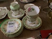 Tea set items arranged including cups, saucers, plates, and a creamer jug with green and gold pattern and pink rose detail on cups.