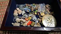 Open jewelry box containing various coins, small figurines, keys, and trinkets.