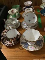 Top view of multiple vintage porcelain demi tasse cups and saucers arranged on a table showing varied floral patterns and gold trim.