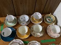 Top view of eight assorted cups and saucers on a wooden surface showing various designs including Royal Albert.