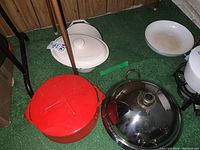 Red Dansk cast iron pot with lid, white covered baking dish behind it, metal frying pan with lid.