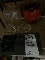Wide view of the lot showing all items on a shelf: clear glass vase, red ceramic pot, two small glass candle holders, black metal candle holder in box