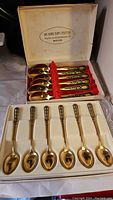 Two boxed sets of espresso spoons, one gold-tone with black decorative handles, one silver marked 830 from David-Andersen.