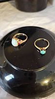 Two gold rings on black round surface; opal and green gemstone rings together.