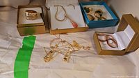 Full view of rings and necklaces arranged in boxes and on paper, showing multiple gold plated 925 sterling silver rings and three necklaces with decorative pendants.