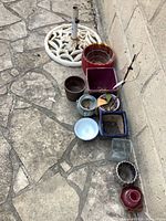 Photo of various worn planter pots and metal painted umbrella stand base placed on stone tile floor against a wall.