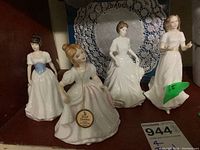 Front view of four Royal Doulton mini figurines on shelf with doilies in background.