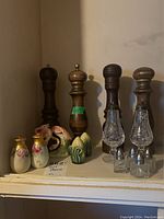 Four sets of wooden shakers with varied wood color and crystal salt containers, along with other ceramic and glass shakers on a shelf