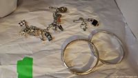 Overview of two silver bangle bracelets, charm bracelet with charms, and necklace with pendant placed on a cloth surface.