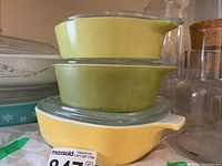 Stacked two vintage Pyrex glass baking dishes in yellow and olive green with glass lids.