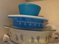 Stacked view of the small blue Pyrex bowl on top of two glass casserole dishes with lids, showing patterns and shapes