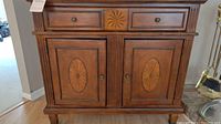 Full front view of brown wood accent cabinet showing two drawers and inlaid doors