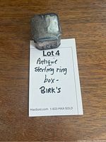 Image of the closed antique sterling silver ring box on a wooden surface with a note showing the lot title.