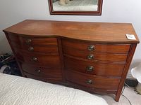 Front full view of the double serpentine dresser showing eight drawers with metal oval handles and the curved front shape.