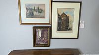 Three framed art pieces on wall: a vintage fishing scene print, a Tudor style building print, and an indoor scene with two men playing a board game.