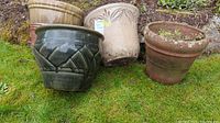 Four medium-sized garden planters - two terra cotta and two glazed ceramic, positioned outdoors on grass.