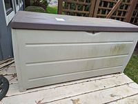 Front view of the large plastic garden storage bin with closed brown lid showing dirt marks and some discoloration.