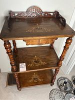 Full view of the three-tier wooden shelving unit with carved back and inlaid floral patterns on each shelf surface.