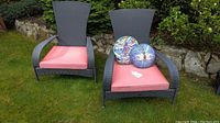 Two grey wicker patio chairs on grass with red cushions and round dragonfly pillows