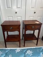 Front view of the pair of wooden bedside tables, showing the drawer and lower shelf on each.