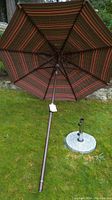 View of the open patio umbrella showing brown and red striped fabric and dark brown metal pole lying on grass.
