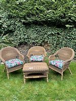 Front view of three wicker chairs with cushions and matching table on grass