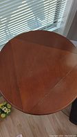 Top view of round drop-leaf wooden end table, shows some chips and surface wear.