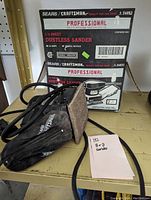 Craftsman 1/4 sheet dustless sander with dust bag and original box on shelf, label visible