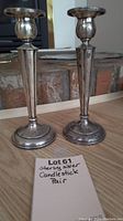 Pair of two sterling silver candlesticks on wooden surface with tag showing lot and description