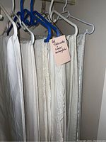 Row of rectangular white and off-white tablecloths and linens hanging on hangers with a label indicating 'Tablecloths Linens rectangular'