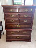 Front view of tall boy dresser showing multiple drawers and brass handles.